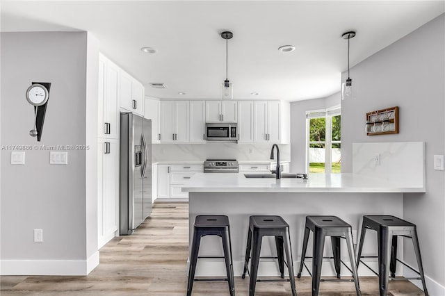 kitchen featuring light countertops, appliances with stainless steel finishes, white cabinets, a sink, and a kitchen bar