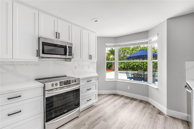 kitchen featuring appliances with stainless steel finishes, light wood-type flooring, white cabinetry, and baseboards