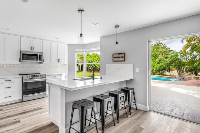 kitchen with a sink, white cabinets, light countertops, appliances with stainless steel finishes, and hanging light fixtures