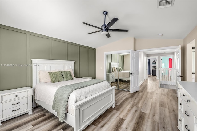 bedroom featuring lofted ceiling, a closet, visible vents, a decorative wall, and light wood-style floors