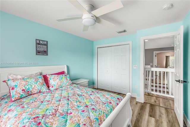 bedroom featuring wood finished floors, visible vents, baseboards, a ceiling fan, and a closet