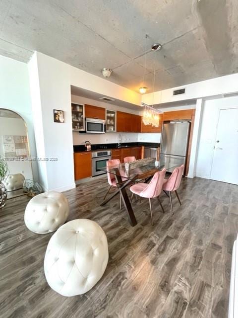 kitchen with arched walkways, dark countertops, dark wood-style flooring, decorative light fixtures, and stainless steel appliances