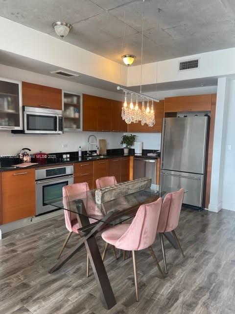 kitchen featuring stainless steel appliances, visible vents, glass insert cabinets, and hanging light fixtures