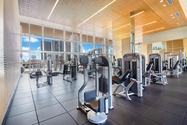 exercise room with wood ceiling, a high ceiling, a wall of windows, and visible vents