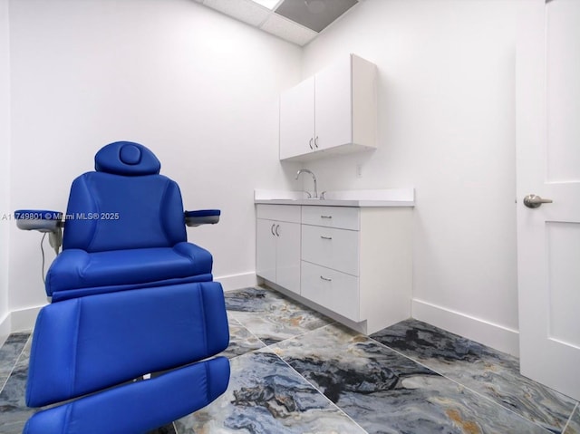 living area with a drop ceiling and baseboards