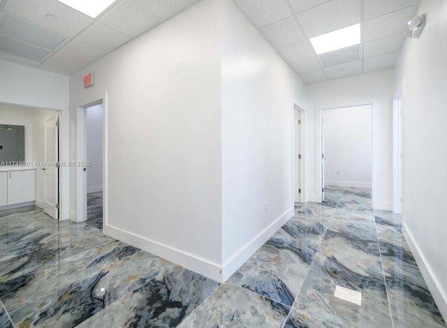 corridor featuring marble finish floor, a drop ceiling, and baseboards