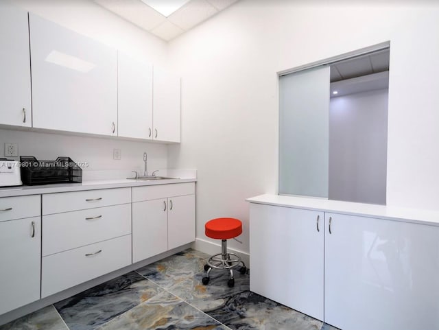 kitchen with baseboards, light countertops, a sink, and white cabinets