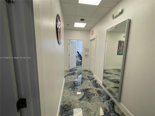 hall with marble finish floor, baseboards, and a drop ceiling