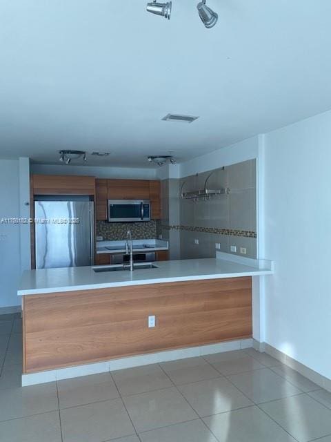 kitchen featuring brown cabinetry, light countertops, stainless steel microwave, and fridge