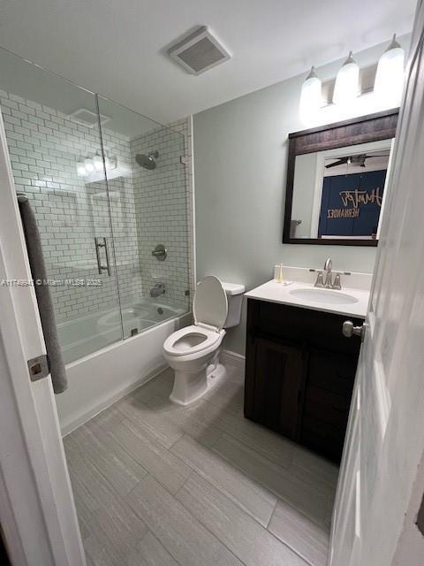 full bathroom featuring baseboards, visible vents, toilet, enclosed tub / shower combo, and vanity