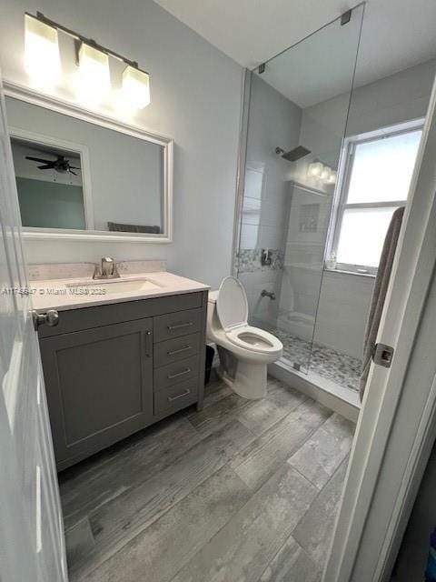 full bath with a ceiling fan, toilet, wood finished floors, vanity, and a shower stall