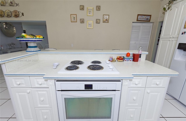kitchen with light countertops, white cabinetry, a peninsula, light tile patterned floors, and white appliances