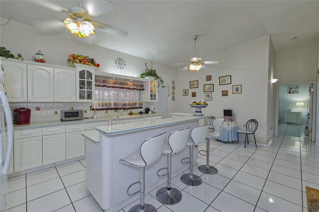 kitchen with light countertops, a kitchen bar, light tile patterned floors, white cabinets, and a ceiling fan