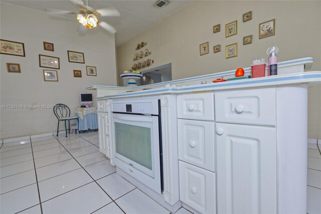 kitchen with light tile patterned flooring, white cabinets, visible vents, oven, and ceiling fan