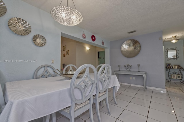dining space featuring light tile patterned flooring, a textured ceiling, baseboards, visible vents, and an inviting chandelier