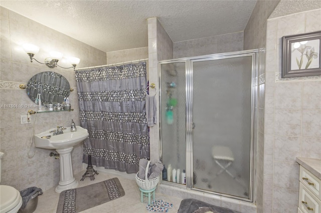 bathroom with a shower stall, a textured ceiling, tile walls, and tile patterned floors