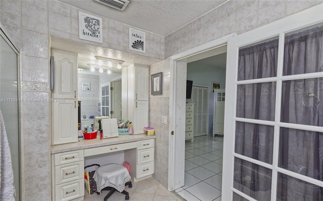 bathroom featuring tile patterned flooring, visible vents, tile walls, and a textured ceiling