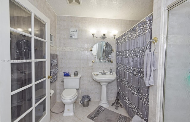 bathroom with tile patterned flooring, tile walls, toilet, a textured ceiling, and curtained shower
