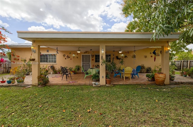 rear view of house featuring stucco siding, a lawn, a ceiling fan, a patio area, and fence