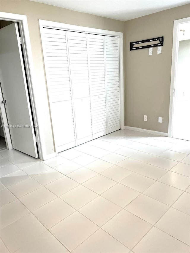 unfurnished bedroom with light tile patterned floors, a closet, and baseboards