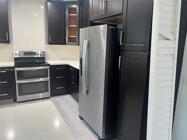 kitchen with light stone countertops, glass insert cabinets, stainless steel appliances, and dark cabinets