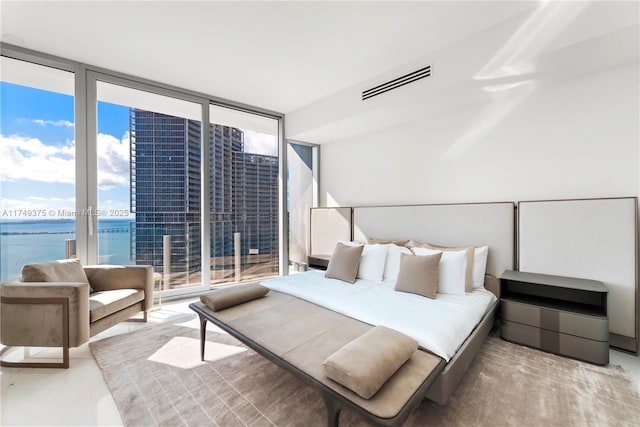 bedroom with a view of city, a water view, visible vents, and floor to ceiling windows