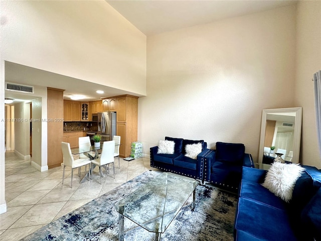 living room featuring light tile patterned floors, a towering ceiling, visible vents, and baseboards