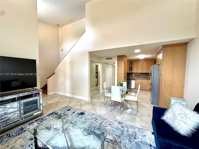 living area with light tile patterned floors, visible vents, a towering ceiling, stairway, and baseboards