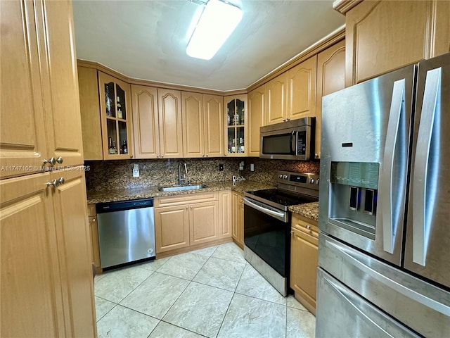 kitchen with dark stone counters, appliances with stainless steel finishes, a sink, and glass insert cabinets