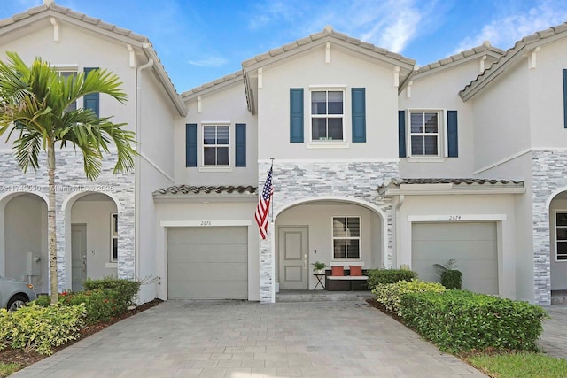 view of front of property with an attached garage, stone siding, a tiled roof, decorative driveway, and stucco siding