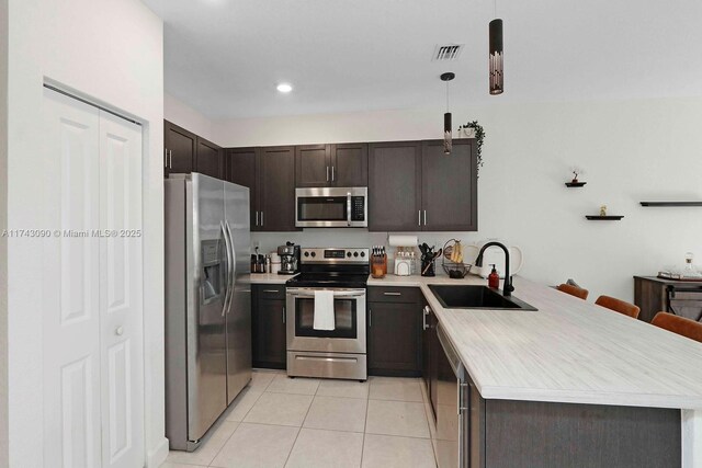 kitchen featuring stainless steel appliances, a peninsula, a sink, hanging light fixtures, and light countertops