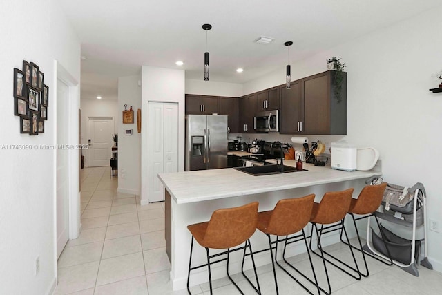 kitchen featuring dark brown cabinetry, a peninsula, stainless steel appliances, light countertops, and a sink