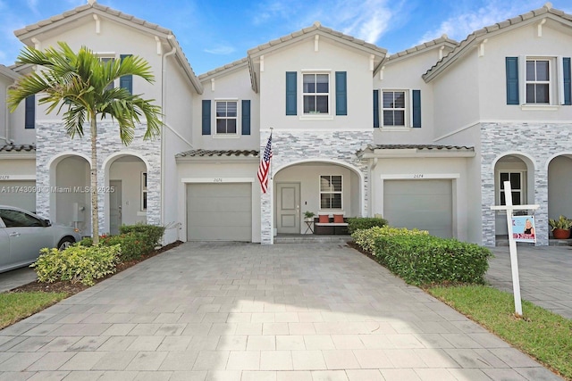 view of front of home with an attached garage, stone siding, a tiled roof, decorative driveway, and stucco siding