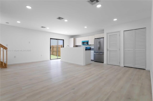 interior space featuring visible vents, white cabinets, open floor plan, freestanding refrigerator, and light wood finished floors