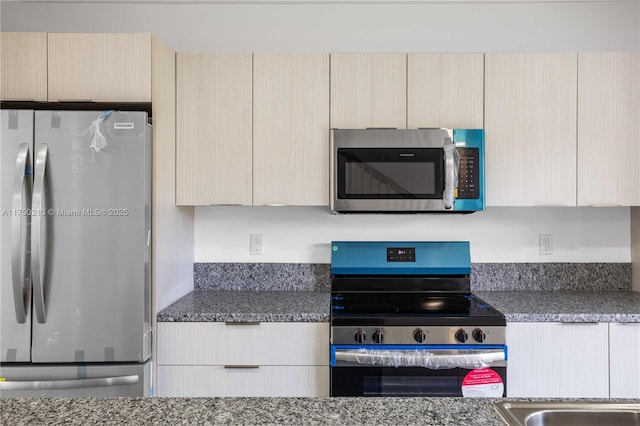 kitchen with dark stone countertops, stainless steel appliances, modern cabinets, and light brown cabinets