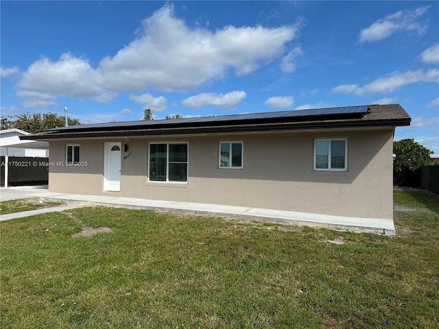 view of front of home featuring fence, a front lawn, solar panels, and stucco siding