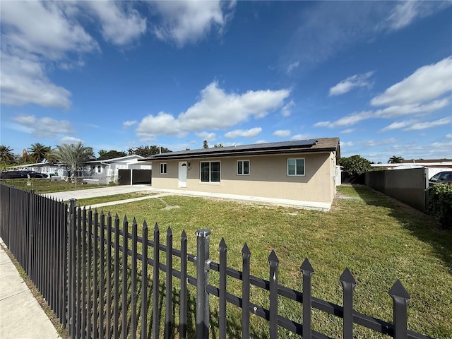 rear view of house featuring a yard, a fenced backyard, roof mounted solar panels, and stucco siding