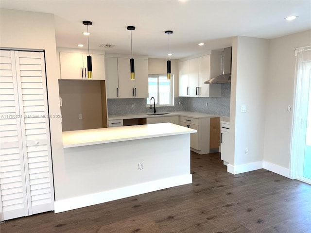 kitchen with decorative light fixtures, dark wood finished floors, light countertops, a sink, and wall chimney exhaust hood