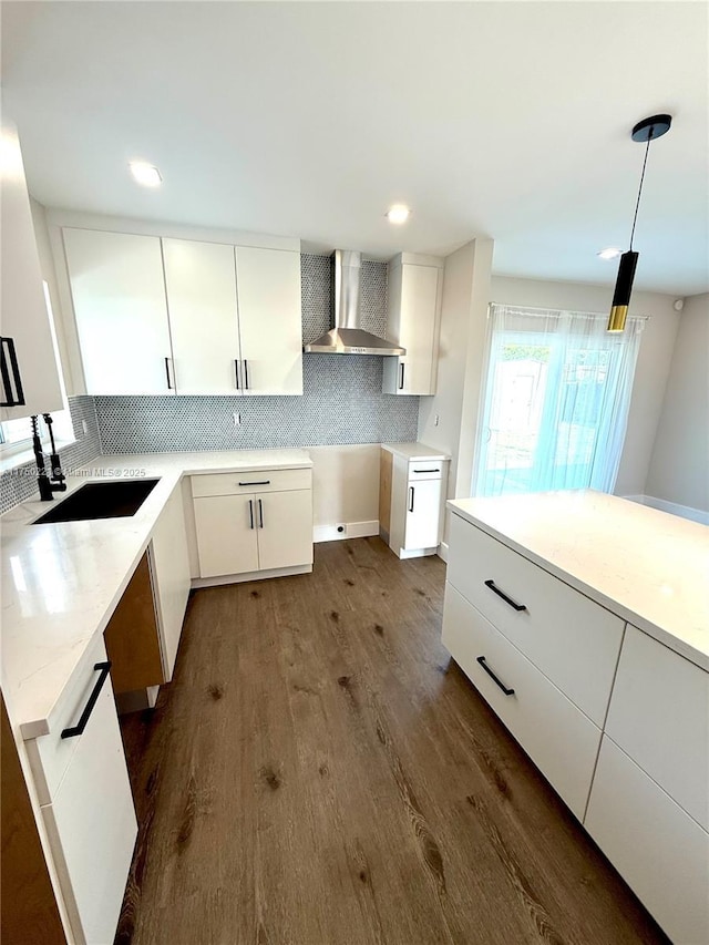 kitchen featuring white cabinets, a sink, hanging light fixtures, and wall chimney exhaust hood