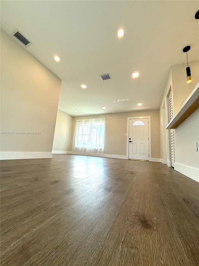 unfurnished living room with dark wood-style flooring, visible vents, and baseboards