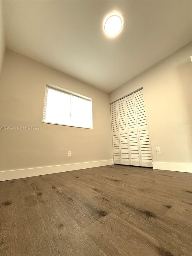 unfurnished bedroom with dark wood-style floors, baseboards, and a closet