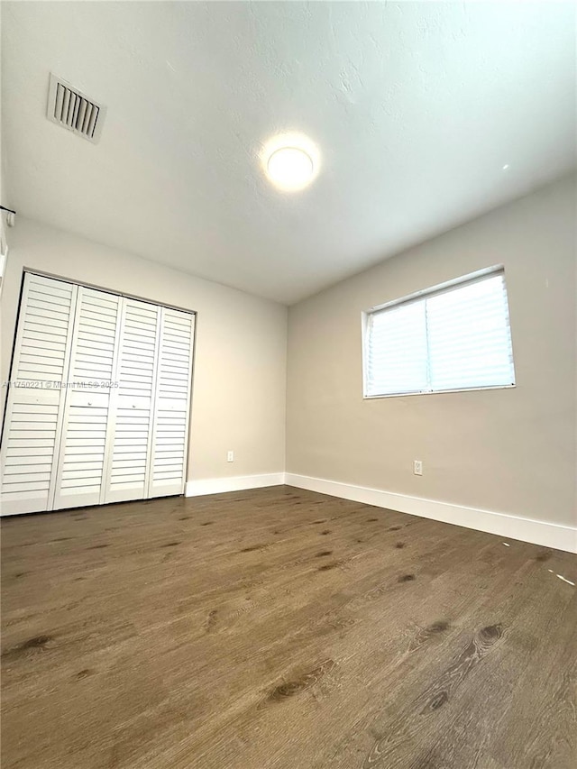 unfurnished bedroom with dark wood-style floors, a closet, visible vents, and baseboards