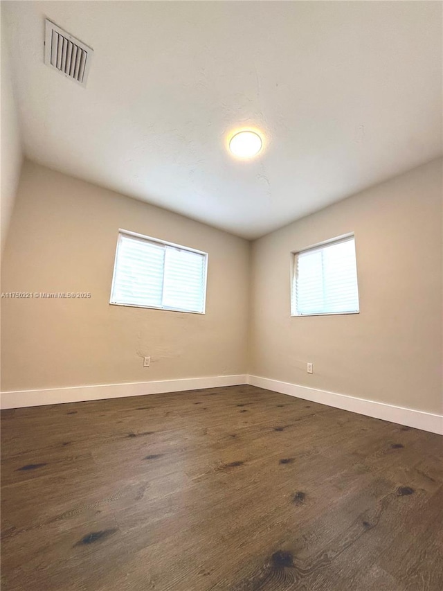 unfurnished room featuring dark wood-type flooring, visible vents, and baseboards