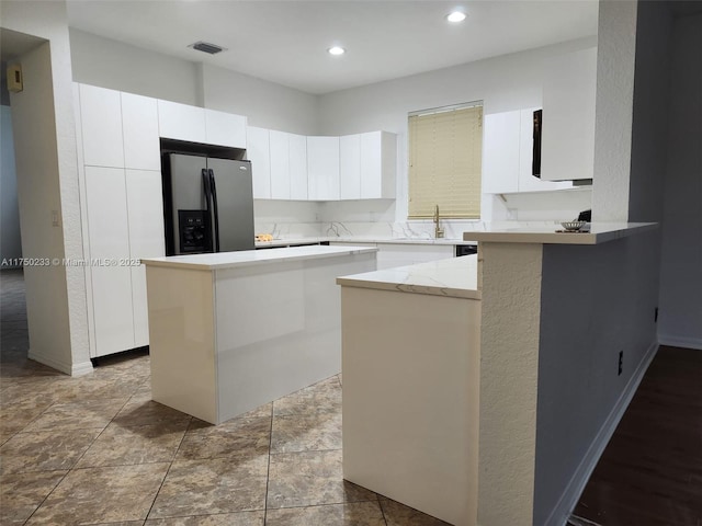 kitchen with recessed lighting, a kitchen island, visible vents, white cabinetry, and stainless steel refrigerator with ice dispenser