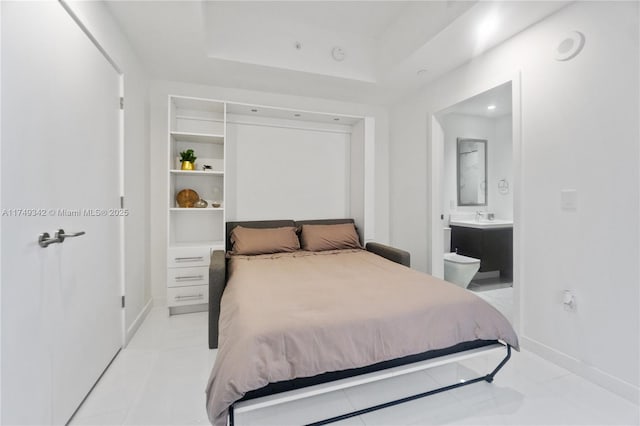 bedroom with ensuite bathroom, a raised ceiling, a sink, and baseboards