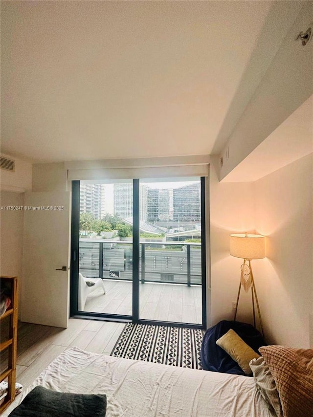 bedroom featuring access to exterior, a city view, light wood-style flooring, and visible vents