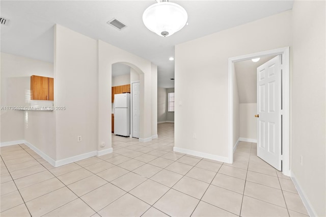 empty room featuring light tile patterned floors, baseboards, visible vents, and arched walkways