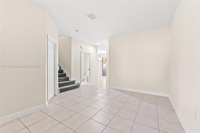 empty room with stairs, light tile patterned floors, visible vents, and baseboards