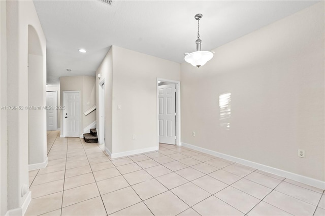 spare room featuring arched walkways, stairway, baseboards, and light tile patterned floors