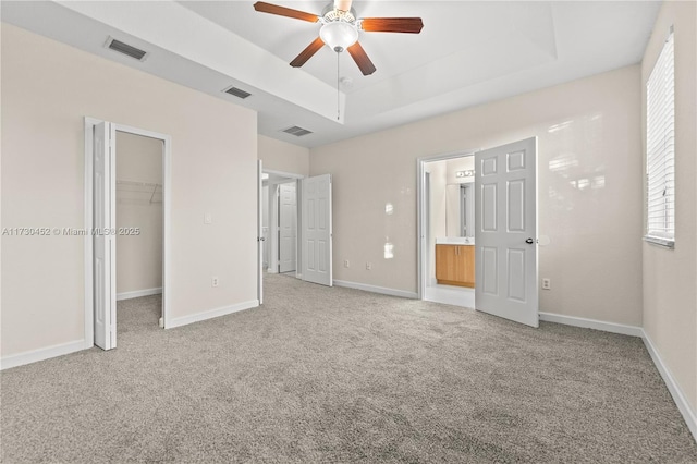 unfurnished bedroom with visible vents, a tray ceiling, baseboards, and light colored carpet